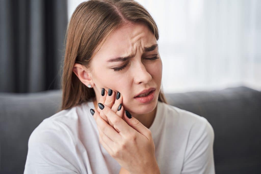 young woman with both hands on her jaw, suffering from severe tooth pain
