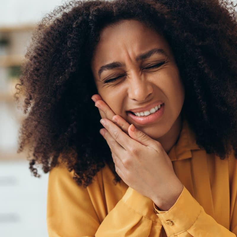 young woman in yellow shirt suffering from tooth pain